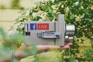 Image of a hand holding up an old video camera with the label Facebook LIVE on it.